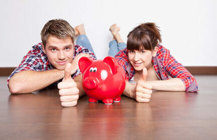 junges Paar, das auf einem Holzboden liegt, mit Keramiksparschwein vor sich