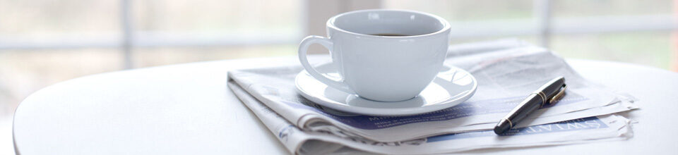 Kaffeetasse und Stift auf zusammengefalteter Zeitung
