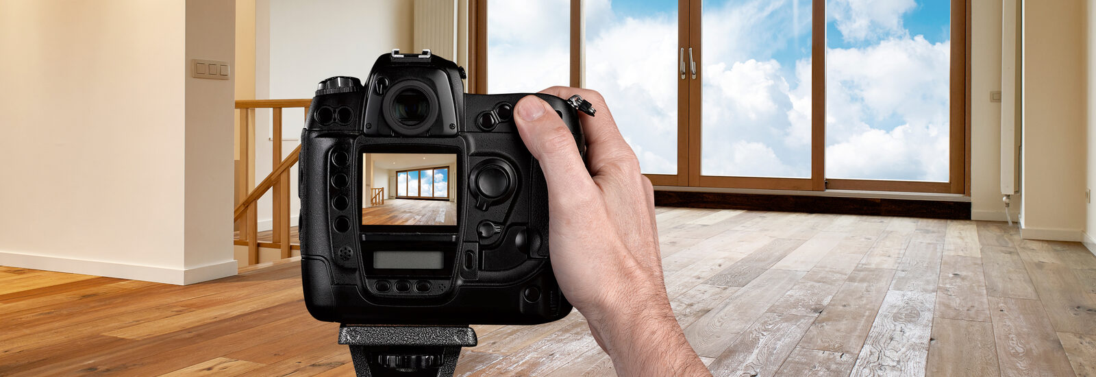 Hand mit Digitalkamera auf Stativ in einem leeren Wohnzimmer.